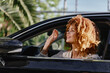© SHOTPRIME STUDIO - smiling woman with curly hair sitting in car window, enjoying sunny day outdoors with green palm trees in background