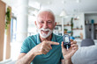 © Graphicroyalty - Successful glucose check. Happy senior man pointing at blood sugar monitor showing normal results. Smiling elderly male with diabetes holding glucometer, healthcare and medicine concept at home.