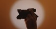 © kinomaster - A silhouette of a hand holding a camera against a warm, softly lit backdrop, capturing the essence of photography. Backstage photo shoot.