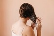 © Meow Creations - Back view of young woman applying white creamy hair mask to wet brown hair on beige background