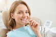 © Meow Creations - Smiling young blonde woman holding clear dental aligner while sitting in dentist chair