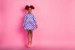 © deagreez - Young girl wearing purple polka dot dress jumping against pink background in a playful fashion lifestyle photo