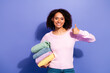 © deagreez - Young woman with pastel sweater holds colorful folded clothes and gives a thumbs up against violet background