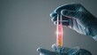 © Landscapers - Gloved hands holding test tube with glowing sample for rare disease research