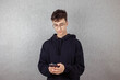 © Natalia - Young guy, student, high school student, typing in smartphone, looking at him on gray background, copy space