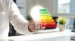© SnapSpark Studios - Hand holding light bulb with energy efficiency rating scale in office environment