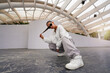 © oscargutzo - Hispanic woman wearing casual sportswear and sunglasses squatting under a white architectural structure