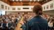 © Macrostock - Medium shot of a speaker addressing a lively crowd in a community hall encouraging public involvement in social initiatives.