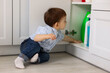 © New Africa - Child safety at home. Little boy opening cabinet with cleaning products in kitchen