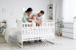 © Pixel-Shot - Happy young family with their cute little baby in crib at home
