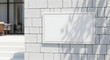 © Nima - Blank horizontal white sign mockup mounted on a modern textured brick wall with natural light and plant shadows.