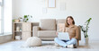 © Pixel-Shot - Young woman using laptop on carpet near grey couch in living room