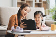 © ARMMY PICCA - A cheerful Asian mother helps her young daughter do homework and color a book at home, while the father works on a laptop in the background. A cozy, bright, and modern family lifestyle.