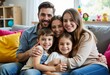 © Michael - A family of five sitting together on a couch with smiles on their faces, embracing each other and posing for the photo in a cozy indoor setting with warm lighting and cheerful expressions