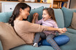 © Graphicroyalty - Happy mother and young daughter playing together on the couch. Smiling woman holding hands with little girl while sitting on sofa. Family fun, playtime, and bonding concept in cozy home interior.