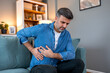 © Graphicroyalty - Side pain and kidney ache. Adult man sitting on sofa and holding painful side with hands. Healthcare and medicine concept. Handsome male suffering from liver, gallbladder or abdominal discomfort.