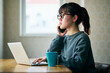 © TY - Young Asian Woman Talking on a Smartphone While Working on a Laptop at Home
