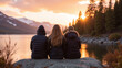 © Oran - Three individuals sit on rock by serene lake, enjoying sunset view. scene captures tranquil moment in nature, surrounded by mountains and trees