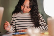 © Studio Marmellata - A young woman with dark, curly hair concentrates on her tablet, holding a stylus in her hand as she works or studies at a desk.