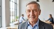 © Soem - A smiling elderly man in a suit, with a blurred background of a conference room.
