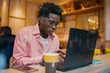 © BullRun - Concentrated African man working on laptop in café, surrounded by tech items, conveying independent digital workflow and remote productivity in urban freelancer lifestyle.