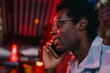 © BullRun - Young man with glasses smiling while talking on smartphone under vibrant red light, reflecting urban tech lifestyle, social connectivity, and confidence through mobile communication.
