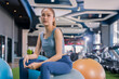 © whyframeshot - confident Asian woman sitting on exercise balls at a modern gym, wearing a gray sports top and blue leggings with white sneakers, posing with a calm and focused look.