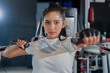 © whyframeshot - fit Asian woman working out at the gym, doing cable machine exercise wearing a gray sports top, showing strength, muscle, and determination in a modern fitness studio.