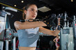 © whyframeshot - fit Asian woman working out at the gym, doing cable machine exercise wearing a gray sports top, showing strength, muscle, and determination in a modern fitness studio.