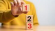 © Newly - A person stacking wooden blocks with numbers on a table in a simple setting with a blurred background