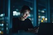 © Serhii - Night-time office scene with a young Asian businesswoman using a laptop and smartphone, glow from screens