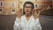 © Krakenimages.com - Senior woman with grey hair gesturing in an urban old town street, wearing glasses and a white shirt, captured in a lively city setting outdoors.