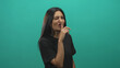 © Krakenimages.com - Woman pressing index finger to lips shushing in studio with teal backdrop and black shirt; playful secrecy.