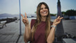 © Krakenimages.com - Woman smiling on a sunny promenade with sea view, making a peace sign, showcasing vibrant outdoor energy, hispanic cultural essence, and youthful joy.
