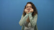 © Krakenimages.com - Young hispanic woman smiling with hands to head in studio against blue wall with curly hair and white tank top; surprise celebration.