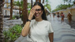 © Krakenimages.com - Woman laughing with hand covering face on a crowded palm tree lined street wearing glasses and white tshirt; carefree joy.