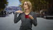 © Krakenimages.com - Woman with glasses and striped shirt blows on red mug of hot coffee on a busy street, hand near mouth cooling gesture, displeased expression; disgust.