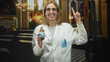 © Krakenimages.com - Woman doctor in white coat holding a syrup bottle, smiling and pointing index finger upward in building interior with pews and chandelier; reassuring care advice.