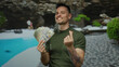 © Krakenimages.com - Man holding us dollars in an outdoor pool resort setting with a playful expression.