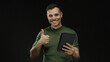 © Krakenimages.com - Hispanic man smiling and holding a tablet against a black background, wearing a green shirt, exuding a positive and confident vibe.