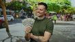 © Krakenimages.com - Young man holding american dollars on an urban street showcases united states banknotes in a sunny, outdoor city environment.