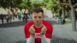 © Krakenimages.com - Young man with a volunteer shirt gestures for money in a sunny park, reflecting a lighthearted scene outdoors with trees in the background.