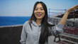 © Krakenimages.com - Young chinese woman smiling at the seaside promenade in an outdoor setting with the blue ocean as a backdrop on a sunny day.