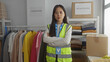 © Krakenimages.com - Young chinese woman in reflective vest volunteering in charity room with folded arms among donations and clothing racks.