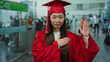 © Krakenimages.com - Woman in red graduation gown taking oath at busy airport terminal surrounded by people and gate signs blending academic and travel themes beautifully.