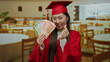 © Krakenimages.com - Woman in graduation gown holding philippine pesos smiling inside a restaurant showcasing success and education.