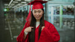 © Krakenimages.com - Woman in red graduation gown smiling in an indoor setting, symbolizing achievement and joy in education and graduation, surrounded by people in a busy environment.