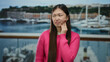 © Krakenimages.com - Woman in pink sweater with toothache at seaside port with boats in the background, expressing discomfort while standing outdoors.