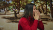 © Krakenimages.com - Young chinese woman shouting in an outdoor park wearing a red sweater, expressing excitement and confidence amidst lush greenery with trees in the background.