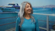 © Krakenimages.com - Senior woman with grey hair smiling by the seaside, standing on a port with a boat in the background, exuding a relaxed outdoor vibe on a sunny day.
